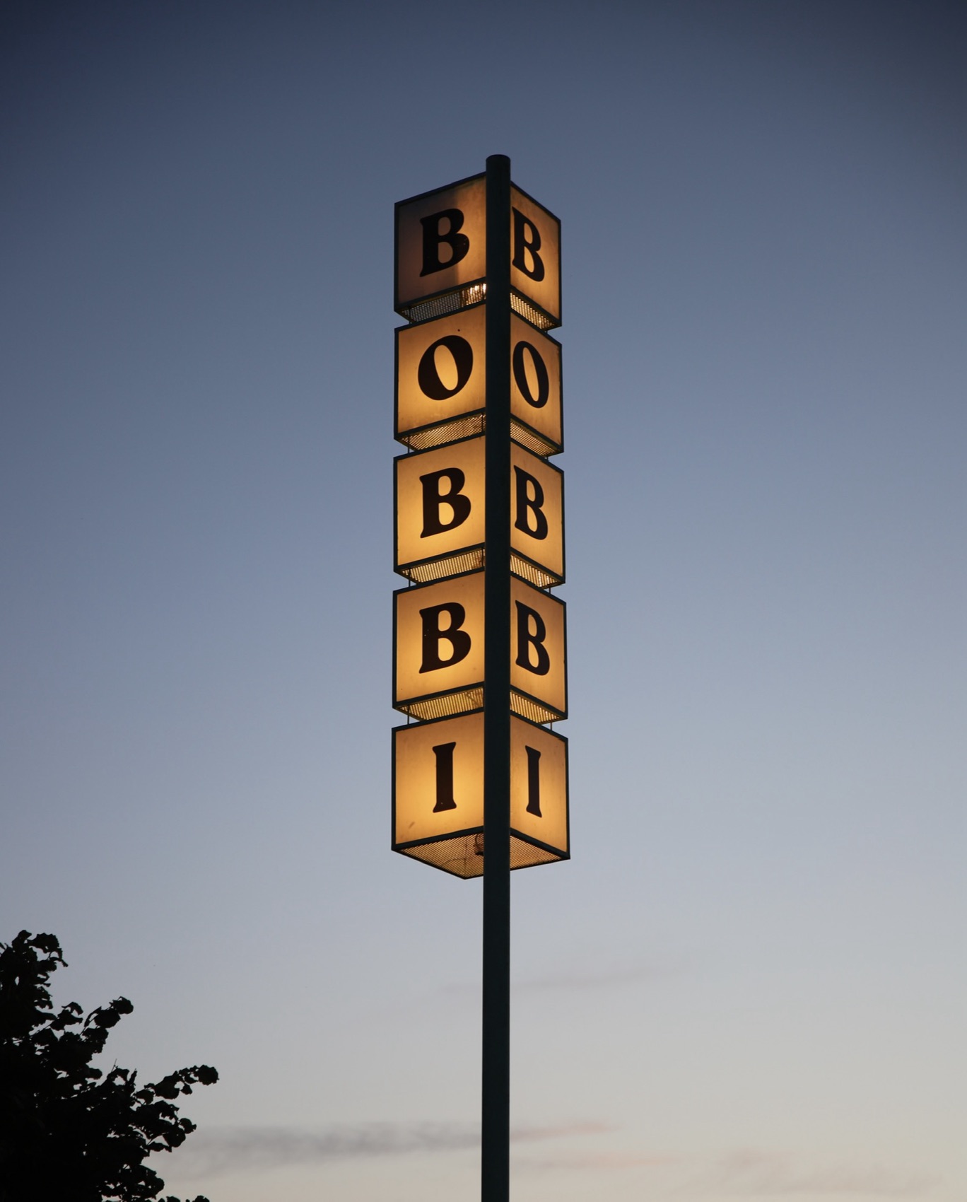 An illuminated stacked sign spelling BOBBI glowing against a deep-blue dusk sky