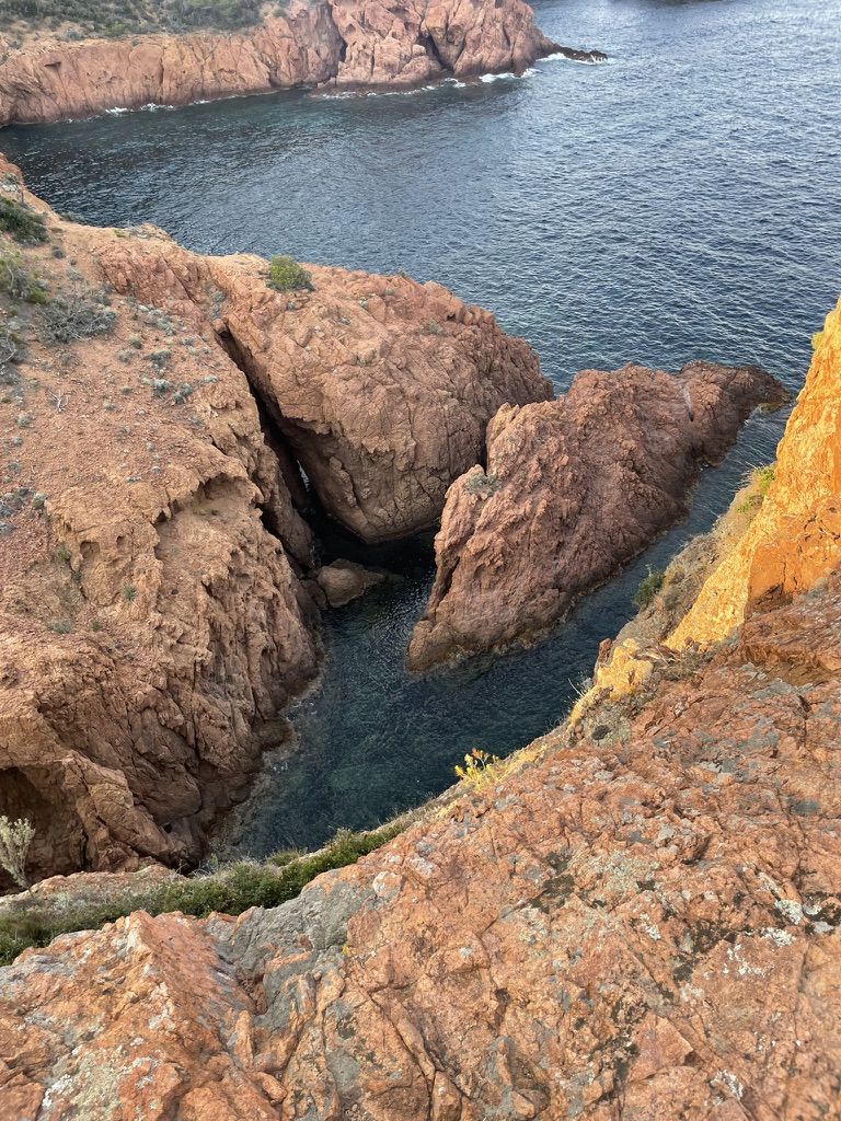 Rust-red cliffs falling to a turquoise cove, seen from above