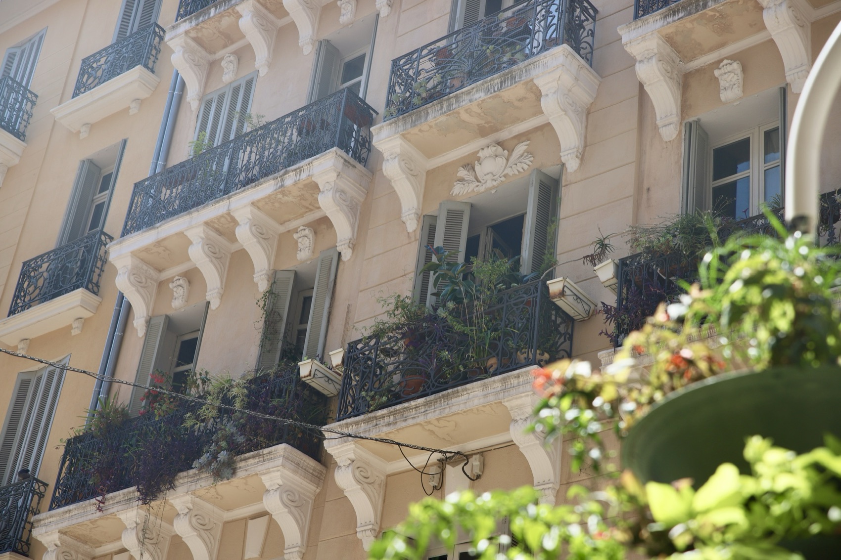 Belle-époque façade with wrought-iron balconies and potted plants on a Mediterranean street